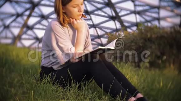 阳光明媚的一天穿着t恤坐在公园草地上读讲稿的年轻少女视频的预览图