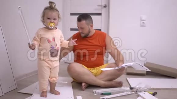 漂亮的胖乎乎的父亲留着胡子女儿正在家里组装一张衣柜床家具是白色的开心快乐视频的预览图