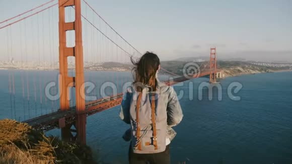 后景相机放大年轻女子背包头发吹在风中欣赏日落在金门大桥视频的预览图