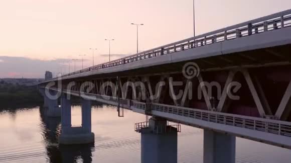 汽车在城市河流的桥上行驶无人机在日落背景下观看桥上的汽车交通城市建筑景观视频的预览图