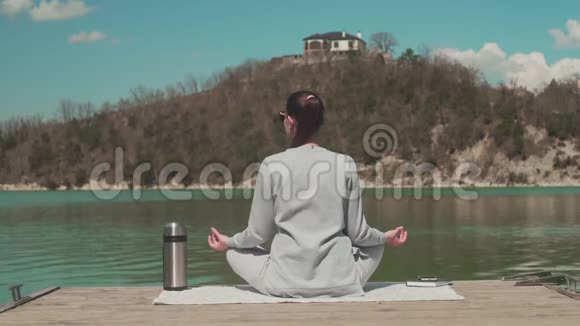 一个女人坐在湖边的木墩上在阳光下冥想在大自然中放松女孩回到框架里视频的预览图