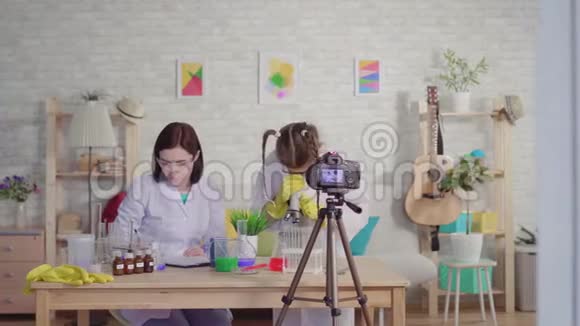 一位女性和十几岁的女孩博客作者在一所学校的化学实验室里通过显微镜进行实验视频的预览图