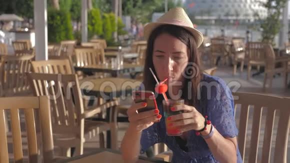 女孩拿着水果鸡尾酒坐在海滩附近的热带咖啡馆里沙滩暑假的概念视频的预览图