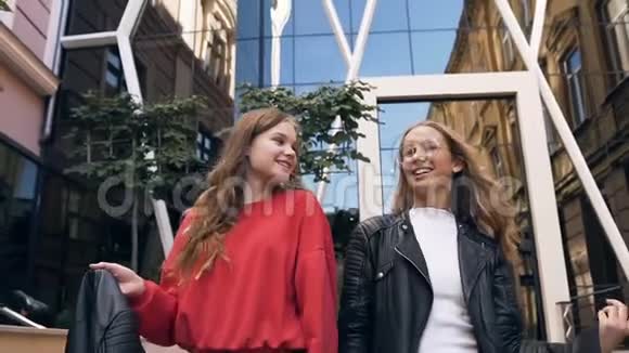 两个开朗时尚的高加索女朋友在现代建筑附近的街道上散步笑着和视频的预览图