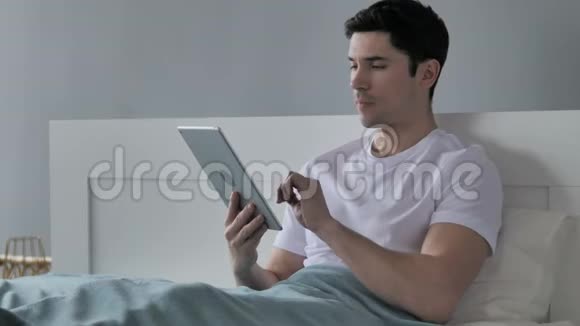 年轻人对成功的反应在床上使用平板电脑视频的预览图