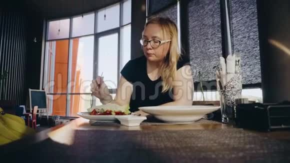 一个女孩在一家漂亮的咖啡馆里吃蔬菜沙拉并与坐在对面的同伴交流对女孩的看法视频的预览图