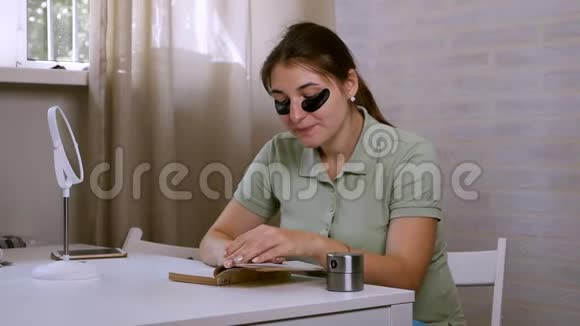 一个年轻的女人眼睛下面有一个黑色的眼罩读一本书用计时器美容护肤视频的预览图