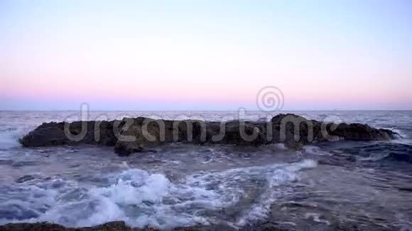 波在地中海上在粉红色的夕阳下撞击岩石视频的预览图