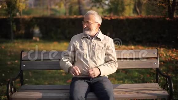 秋天公园里白发苍苍的老人在长凳上休息老人微笑视频的预览图