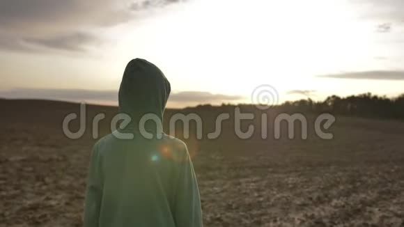 在日落后的景色中一个戴着兜帽的男孩沿着田野散步视频的预览图