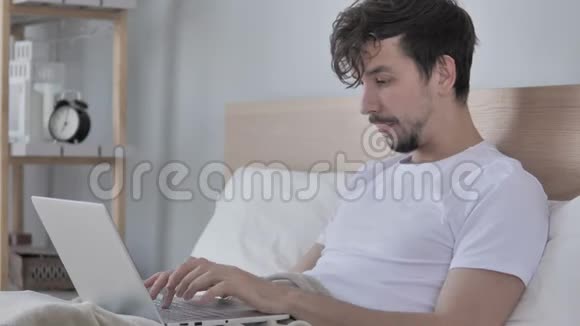 伤心的年轻人在床上使用笔记本电脑时面临损失视频的预览图