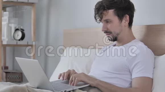 兴奋的男人躺在床上在线视频聊天视频的预览图