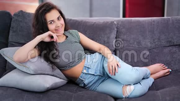 快乐的年轻休闲赤脚妇女摆着放松的姿势躺在家里的沙发上全镜头视频的预览图