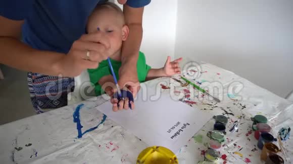 妈妈和小男孩用水彩画在纸上做掌纹万向节运动视频的预览图