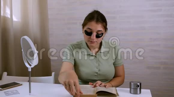 一个年轻的女人眼睛下面有一个黑色的眼罩读一本书用计时器美容护肤视频的预览图