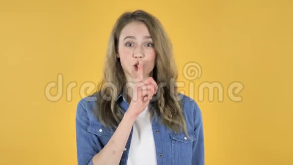 沉默的年轻漂亮女孩嘴唇上的手指黄色背景视频的预览图