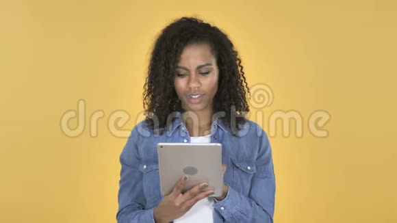 非洲女孩为成功而兴奋同时使用黄色背景下的平板电脑视频的预览图