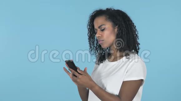 蓝色背景下使用智能手机时震惊的非洲女孩视频的预览图