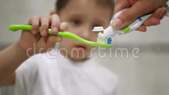 特写一个小男孩的脸他拿着牙刷刷牙妈妈把白色牙膏穿上视频的预览图