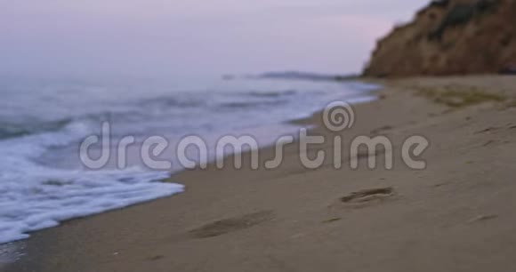 沙滩上的泡沫海浪拍打着沙滩正被海水拉回远处有悬崖峭壁视频的预览图