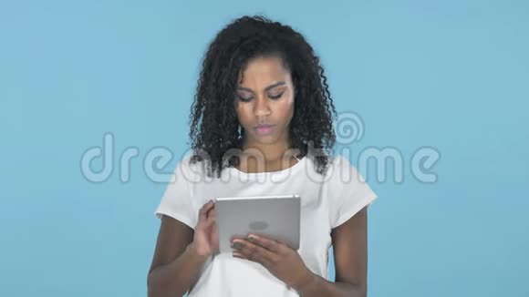 非洲女孩在蓝色背景下使用平板电脑时浏览互联网视频的预览图