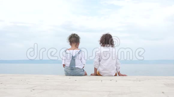 男孩和女孩在清澈的大海的岸边坐着看着远处快乐的孩子旅游理念视频的预览图