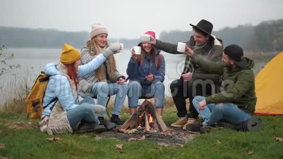 快乐的年轻人朋友们在森林里围着火堆喝着温暖的棉花糖视频的预览图