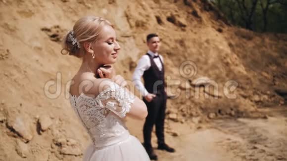 一个穿着雪白裙子的漂亮女孩手指轻轻地沿着她的脖子它站在沙堆的背景下视频的预览图