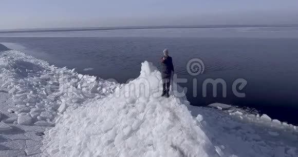 鸟瞰年轻活跃的快乐男子停留在冰冰冰川附近的冬季海洋海岸线医生飞进了视频的预览图