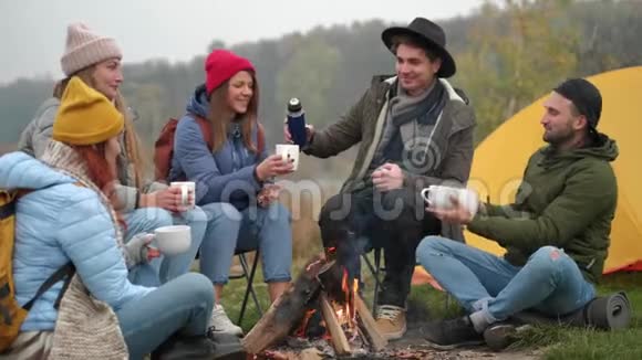 朋友们围着温暖的棉花糖坐在森林里的火堆里喝着饮料叮叮当当视频的预览图