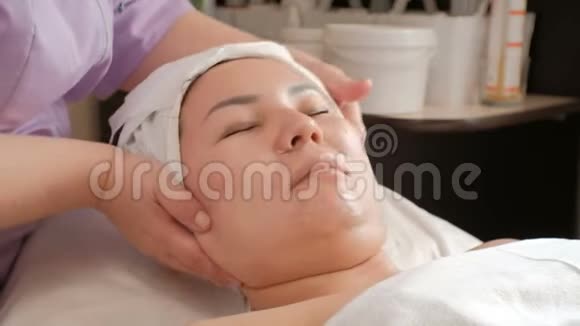 亚洲女孩的面部按摩美容师双手特写转向女性头部的侧面视频的预览图