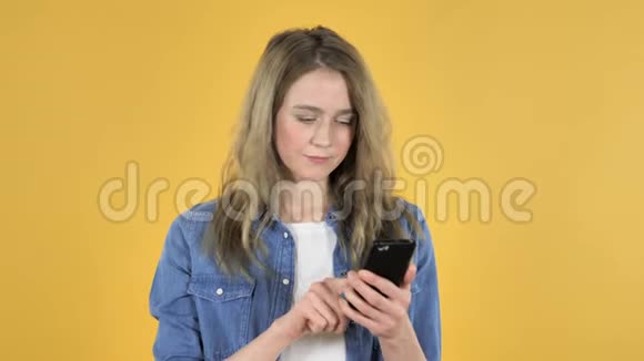 年轻漂亮的女孩在黄色背景下使用智能手机时为成功而兴奋视频的预览图