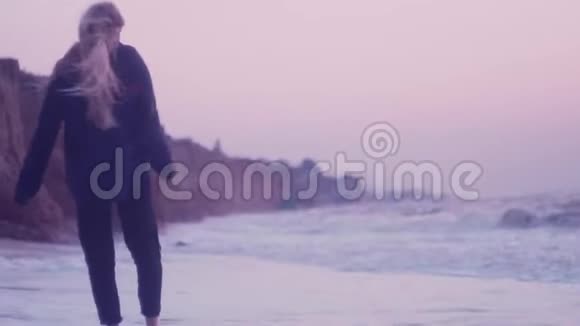 黎明时女孩走在潮湿的沙滩上触摸海浪中的泡沫视频的预览图