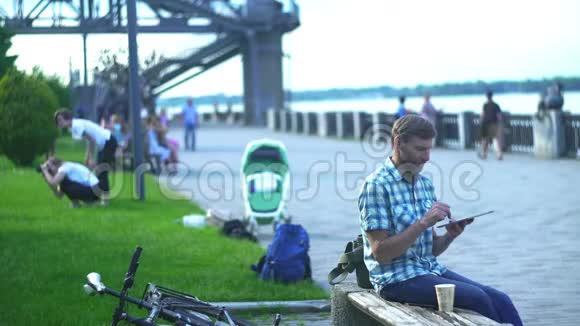 成熟的男人在数字平板电脑上浏览坐在公园的长凳上视频的预览图