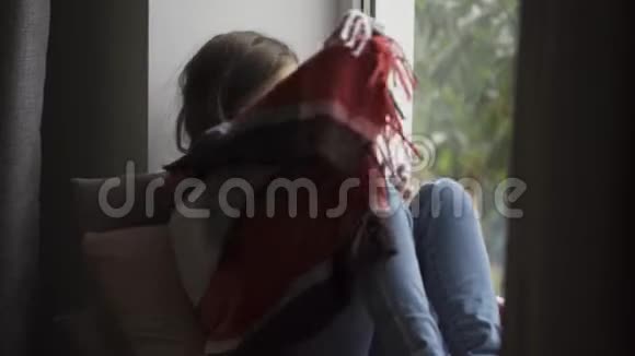 生病的黑发女孩被温暖的毯子覆盖在家的窗台上白种人发烧的孩子看着视频的预览图