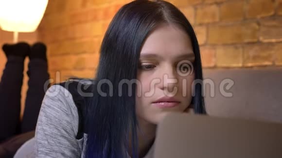 在舒适的家中躺在沙发上用笔记本电脑阅读电子书的年轻白种人女性特写镜头视频的预览图