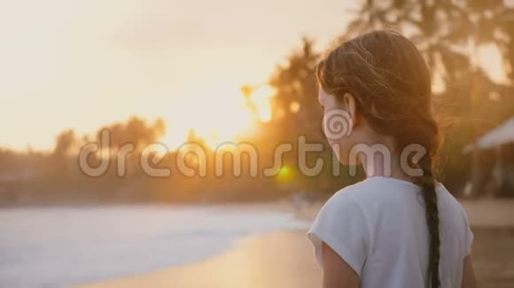 快乐放松的小女孩68岁头发随风飘动站在异国情调的海边看日落视频的预览图