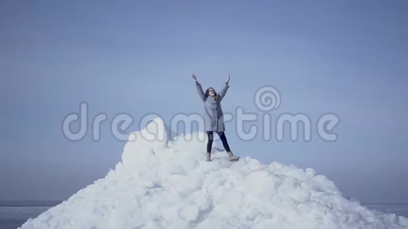 金发女人穿着温暖的外套站在冰川顶部举起双手凯旋而归令人惊叹的景色视频的预览图