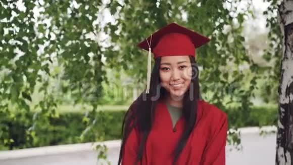 漂亮的亚洲女孩成功毕业学生的肖像穿着长袍站在校园里微笑着视频的预览图