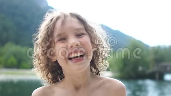 一个美丽的卷发男孩在山湖景色的背景上的近距离肖像快乐的孩子在夏天休息视频的预览图
