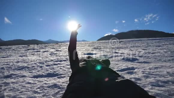 无法辨认的人躺在雪地草地上在阳光明媚的日子里用手指看着灿烂的太阳男性手视频的预览图