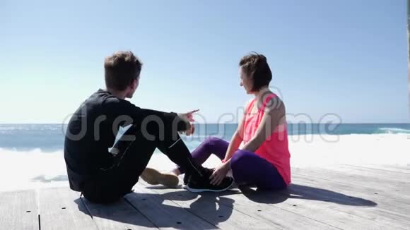 年轻的男人和女人坐在岩石海滩上男朋友用手指指着海和天空说话视频的预览图