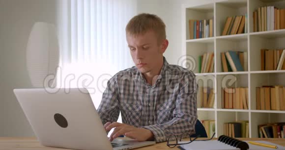 高加索商人在书架背景上专心地使用笔记本电脑的肖像视频的预览图