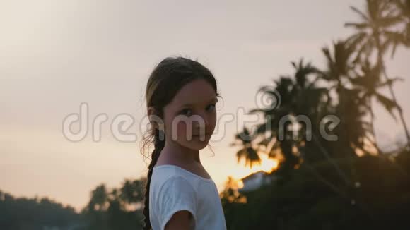 快乐轻松的小68岁的女孩子回头看镜头在夕阳下的热带海滨度假视频的预览图