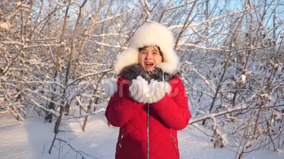 小女孩从手里吹起雪花在冬天的公园里被夕阳照亮特写镜头快乐女孩吹雪花视频的预览图