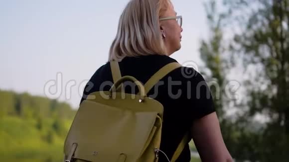一个背着包的女孩沿着河堤朝她的方向看运动后视视频的预览图