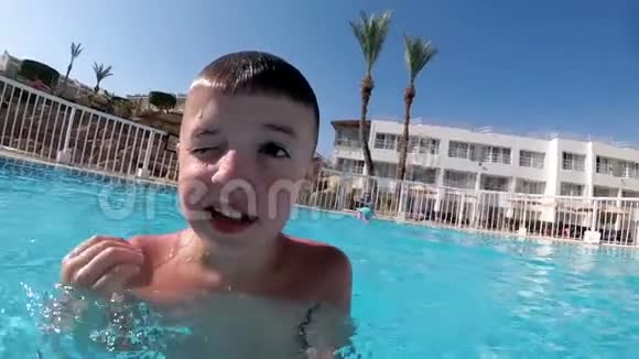 快乐的男孩与一个滑稽的脸采取自己的视频自拍相机在游泳池视频的预览图