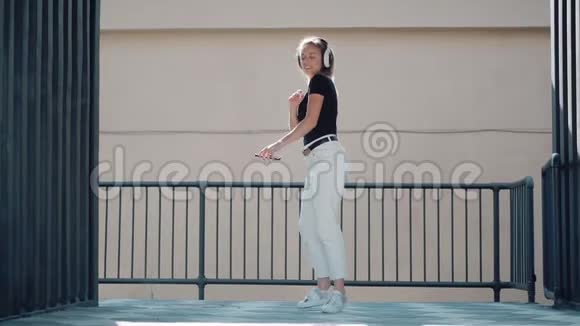 年轻女子在户外听耳机音乐时欢快地跳舞跳得很高视频的预览图