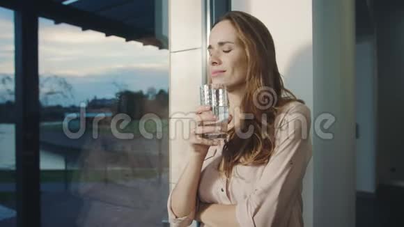 放松的女人在全景窗口附近喝水口渴的女士喝水视频的预览图