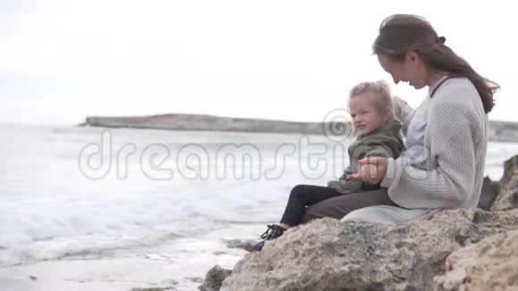 妈妈和她的小女儿正坐在海边的岩石上聊天视频的预览图